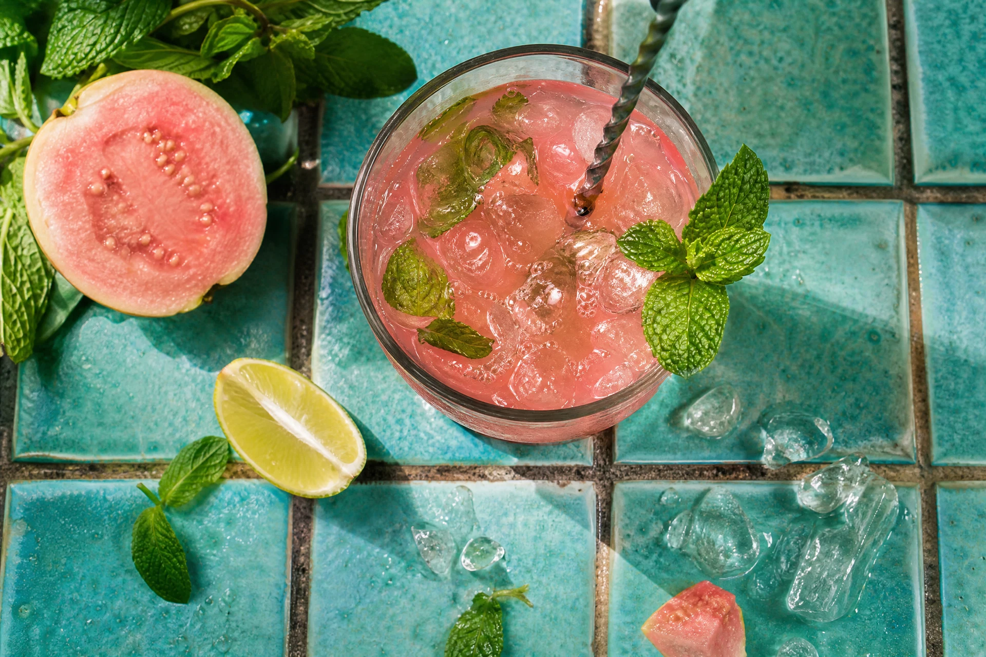 Top-down view of a guava and lime mocktail on a wooden table with fresh ingredients scattered around.