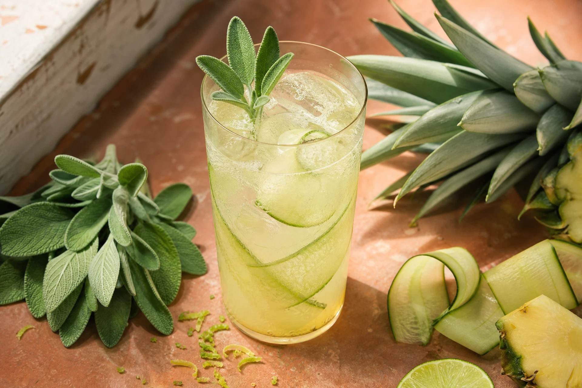 Close-up of fresh sage leaves and pineapple slices next to a refreshing green-tinted mocktail.