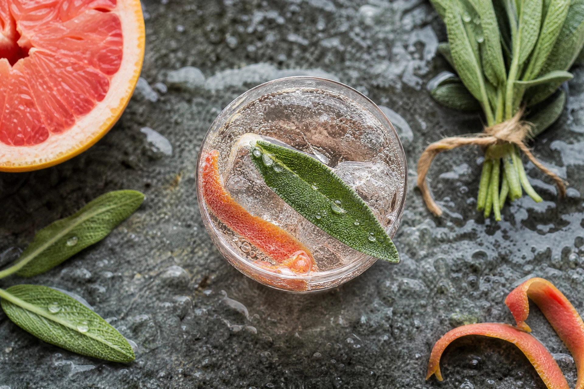 Top-down view of a sage-infused mocktail featuring vibrant ruby grapefruit peel and bubbling mineral water.