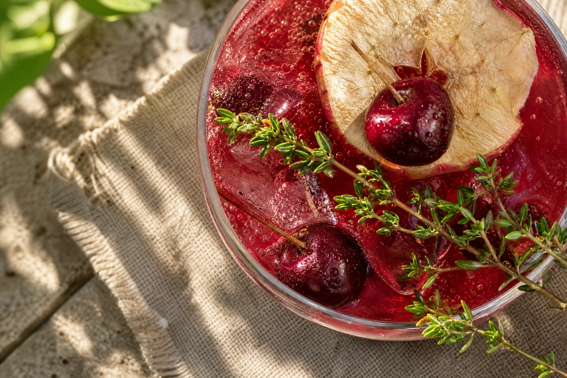 Fresh thyme, tart cherry juice, apple juice, and lemon arranged beside a chilled zero-proof mocktail.