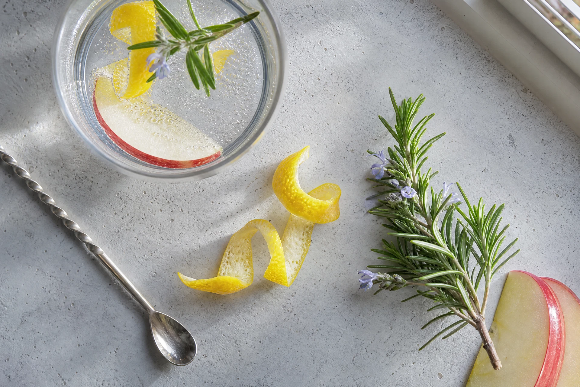 Close-up of fresh Meyer lemons and rosemary sprigs next to a bottle of sparkling mineral water.